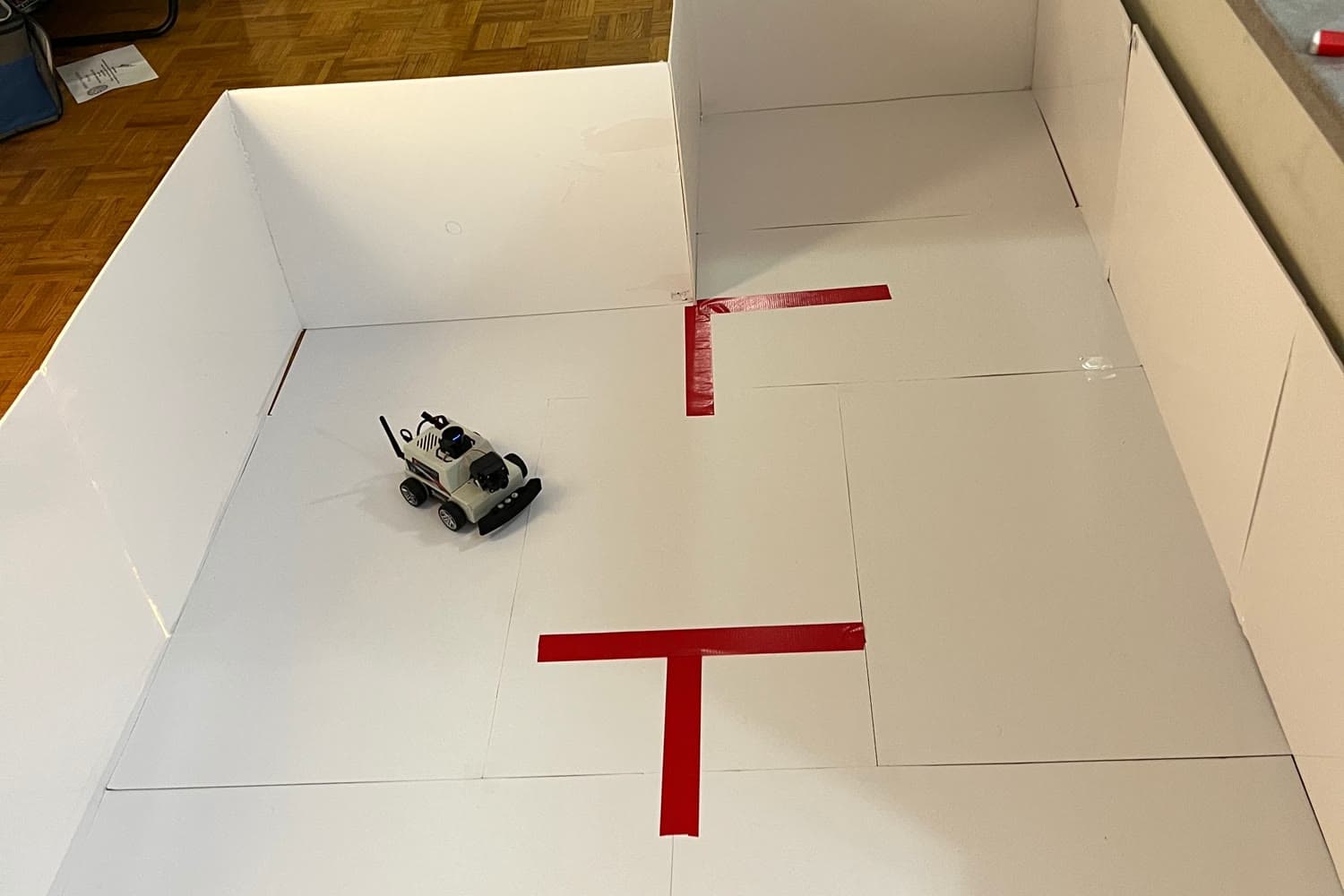 The assistive-navigation robot on its taped test course, red-tape waypoint markers on a white foam-board floor